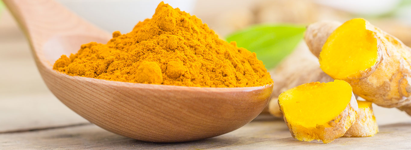 Ground turmeric on a wooden spoon beside fresh root